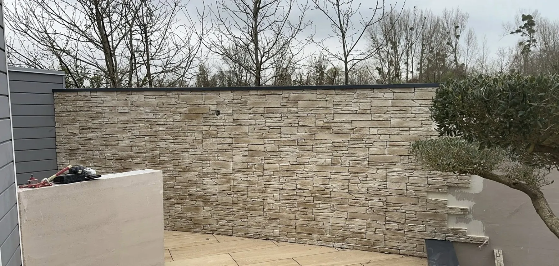 Mur de clôture habillé en parement pierre avec couvertine, en bordure d'une terrasse en bois composite
