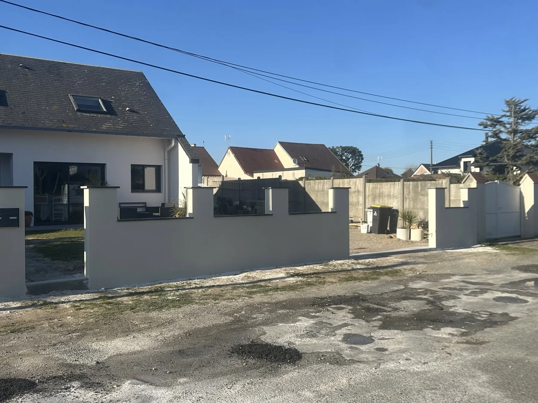 Mur de clôture enduit blanc avec piliers et couvertines noires devant une maison