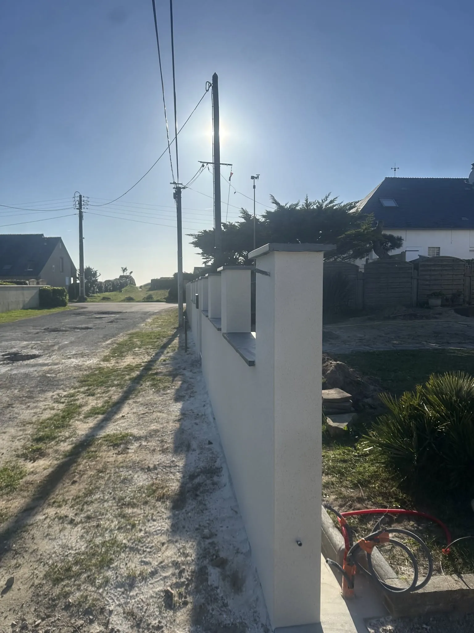 Muret de clôture enduit avec piliers et couvertines, vu en enfilade le long de la voie