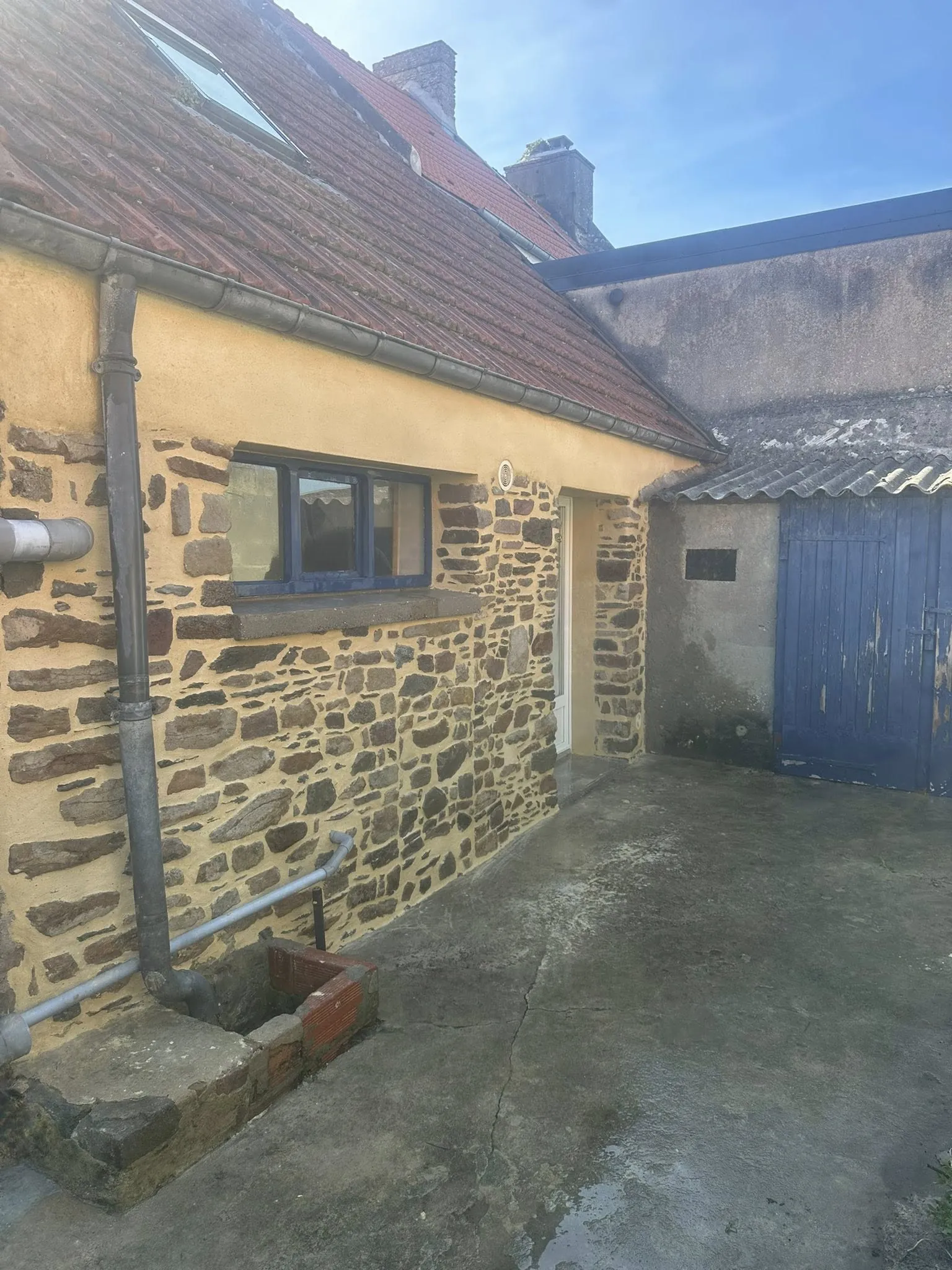 Façade de maison ancienne mêant pierre apparente et enduit à la chaux teinté, avec cour en béton